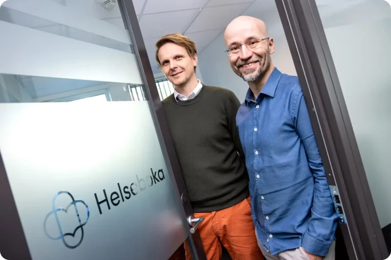 Two members of the Helseboka team at the door of the Helseboka office